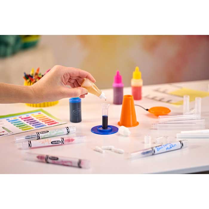 Marker Workshop. Child putting dye drops in beaker on table surrounded by marker workshop parts.